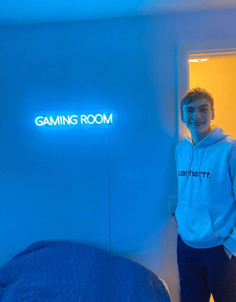 Dreng står på sit gamer værelse med sit nye gaming neonskilt hvor der står gamingroom